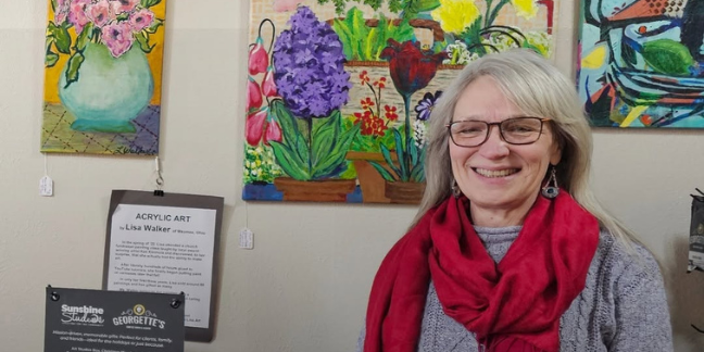 A woman in a red scarf smiling in front of a series of canvas paintings